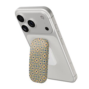 Può includere: Uno smartphone argentato con un supporto per telefono a fantasia attaccato. L'impugnatura presenta un motivo geometrico ripetuto nelle tonalità del giallo, verde e blu navy. Il telefono è angolato, mostrando le sue lenti.