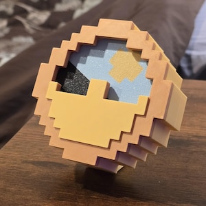 May include: A pixelated 3D printed sculpture of a face with a yellow background, blue and white eyes, and a black eye patch.