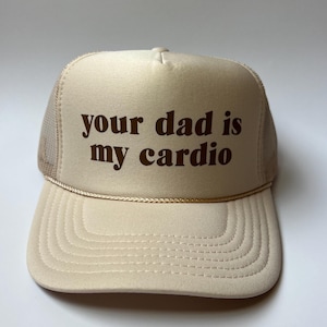 Peut inclure: Casquette de camionneur beige avec l'inscription "your dad is my cardio" en marron. Le chapeau a un dos en filet, une visière incurvée et un cordon décoratif. Un accessoire de mode.