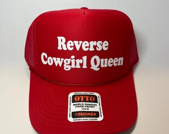 May include: A red trucker hat featuring the white text "Reverse Cowgirl Queen". The hat has a foam front and a mesh back. A label on the hat reads "OTTO" and "Trucker".