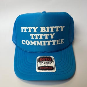 Puede incluir: Una gorra de camionero azul brillante con una parte posterior de malla blanca. La parte delantera de la gorra tiene texto blanco que dice "itty bitty titty committee". La gorra tiene una etiqueta negra con texto blanco que dice "Otto World Famous Foam Front OSFM Trucker Durable Snap Closure".