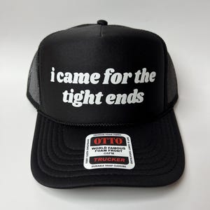 Könnte beinhalten: Schwarze Trucker-Cap mit dem weißen Text "i came for the tight ends". Die Kappe hat eine Mesh-Rückseite und einen gebogenen Schirm. Das Etikett lautet "OTTO WORLD FAMOUS FOAM FRONT TRUCKER".