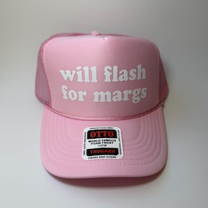 May include: Pink trucker hat with the text "will flash for margs" in white. The hat has a mesh back and a curved brim. The hat also has a tag that says "OTTO WORLD FAMOUS FOAM FRONT OSFM TRUCKER DURABLE SNAP CLOSURE".