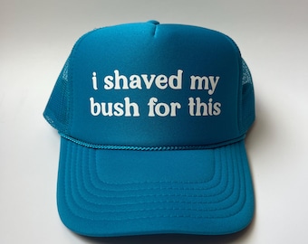 Peut inclure: Un chapeau de camionneur bleu turquoise avec un filet blanc à l'arrière. Le devant du chapeau est orné d'un texte blanc qui dit "i shaved my bush for this".