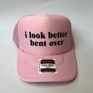 May include: Pink trucker hat with a black mesh back and a white label that says "OTTO World Famous Foam Front OSFM Trucker Durable Snap Closure". The front of the hat has black text that says "i look better bent over".