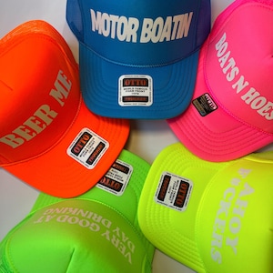 May include: Five neon colored trucker hats with mesh back panels. The hats have different phrases printed on the front in white lettering. The phrases are "Motor Boatin", "Beer Me", "Boats N Hoes", "Very Good At Day Drinking", and "Ahoy  Truckers".