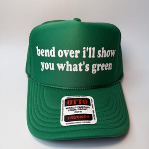 Op de afbeelding: Groene truckerpet met de tekst "bend over I'll show you what's green" in het wit. De pet heeft een schuimrubberen voorkant en een zweetband van badstof. Met druksluiting.