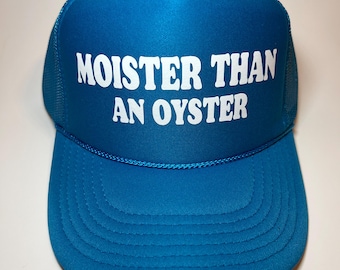 Peut inclure: Un chapeau de camionneur bleu turquoise avec un filet blanc à l'arrière. Le devant du chapeau porte le texte "MOISTER THAN AN OYSTER" en blanc.