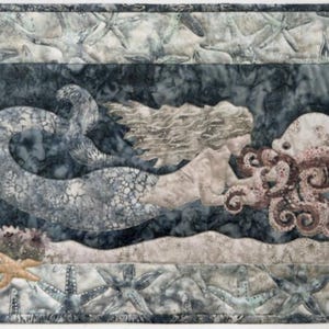 May include: A quilted wall hanging featuring a mermaid with an octopus. The mermaid has flowing hair and a patterned tail. The octopus is a light brown color. The background is a dark blue with a quilted border. Coral and starfish are also visible.
