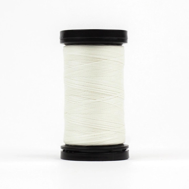 May include: A spool of white thread with a black plastic top and bottom.