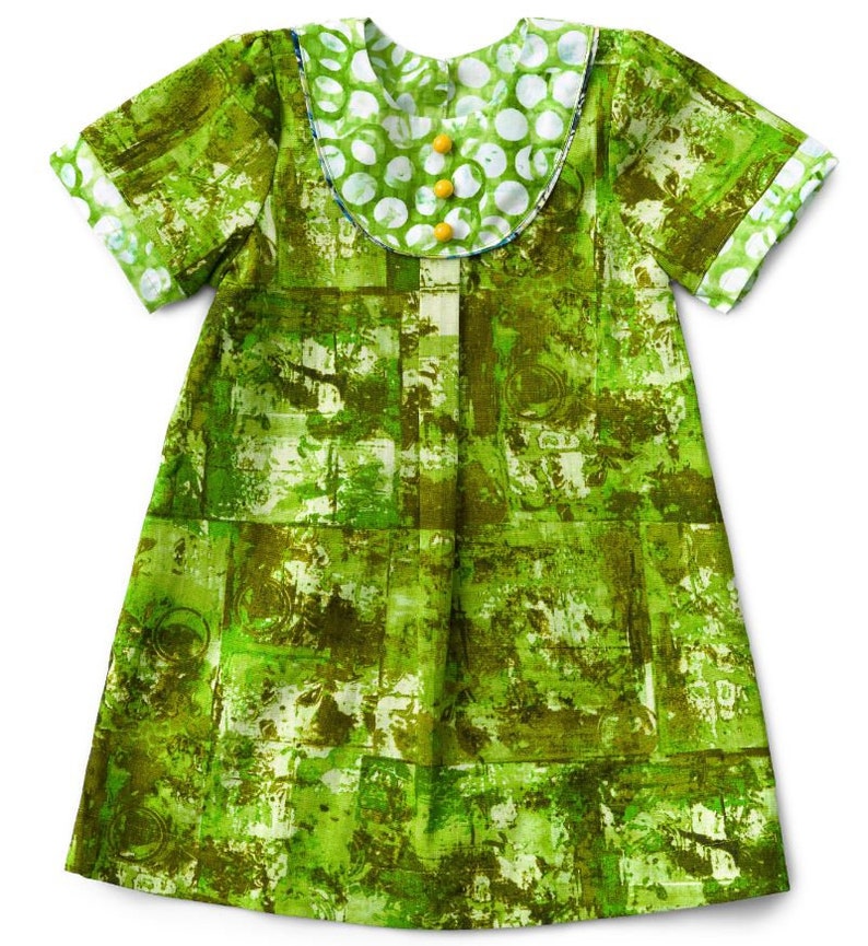 May include: A green and white patterned dress with short sleeves and a white collar with polka dots. The collar has yellow buttons.
