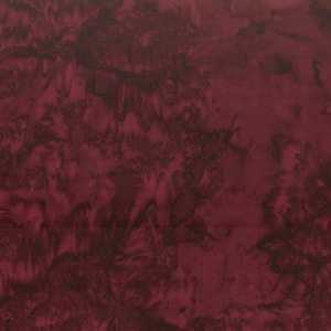 May include: A close-up of a burgundy fabric with a marbled effect. The fabric has dark, swirling patterns throughout, creating a textured appearance. The color is a deep, rich shade of red.