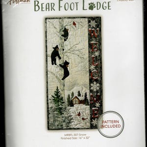 May include: A fabric kit titled "Bear Foot Lodge" featuring a winter scene with black bears climbing a tree. The quilt design includes a snowy landscape with a cabin and the word "WELCOME". Finished size is 40.6 cm x 81.3 cm.