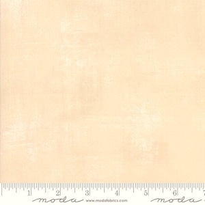 May include: A light peach-coloured fabric with a textured finish. A ruler is along the bottom edge, with the word "moda" printed on it. The website address www.modafabrics.com is also visible. The fabric is suitable for various craft projects.