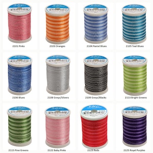May include: Twelve spools of Sulky 100% rayon thread arranged in a grid. Each spool features a distinct color including pink, orange, blue, teal, silver, black, green, and purple. Labels on top display the brand name and color codes.