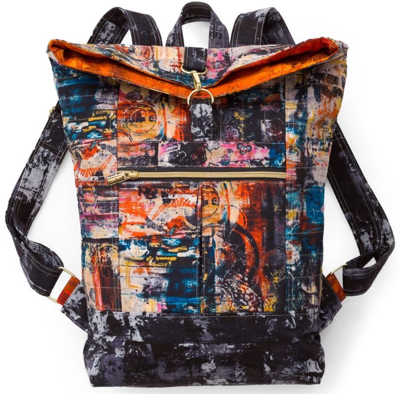 May include: A black canvas backpack with a large flap and a zippered pocket. The backpack has a colorful abstract print with orange, blue, and yellow accents.