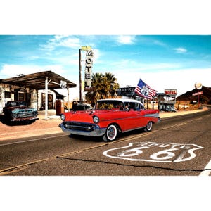 May include: A red classic car drives down Route 66, a classic American highway. The car is a 1957 Chevrolet Bel Air, with a white roof and chrome accents. The car is driving past a motel and a gas station, with a sign for Route 66 in the background.