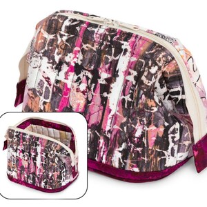 May include: A quilted makeup bag with a pink, brown, and white abstract print. The bag has a zipper closure and a burgundy velvet trim.