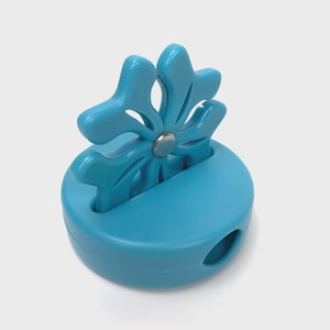 May include: A blue plastic pencil sharpener with a flower-shaped top. The sharpener has a small hole for sharpening pencils and a metal blade inside.