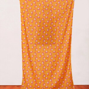 May include: A yellow fabric with a repeating pattern of pink and purple unicorn heads. The fabric is being held up by a person's hands.
