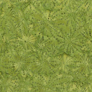 May include: A light green fabric featuring a batik-style pattern of small, dark green circular dots and organic, mottled shapes. The surface has a textured appearance with varying shades of lime and olive green creating a layered, dappled effect.