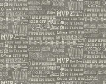 May include: A dark grey fabric featuring a repeating pattern of white distressed text related to American football. Phrases include T-O-U-C-H-D-O-W-N, WIN, MVP, TACKLE, DEFENSE, KICK OFF, PUNT, FIRST AND TEN, GAME DAY, BLITZ, and TAILGATE PARTY.