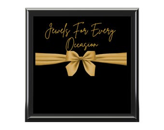 May include: Black framed sign with gold text that reads "Jewels For Every Occasion" and a gold bow.