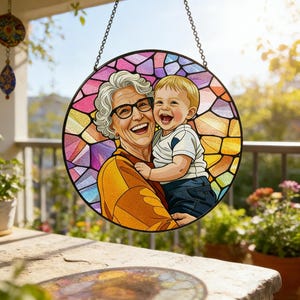 May include: A round stained glass window featuring a smiling woman wearing glasses holding a laughing baby. The background is a colorful mosaic pattern. The window is hanging from a chain.