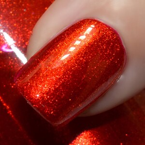 May include: Close-up of a fingernail painted with a vibrant, shimmering red nail polish. The polish has a glittery finish, reflecting light. The nail is next to a bottle of the same red nail polish.