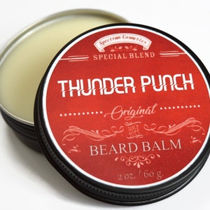 May include: A red tin with a black lid containing a beard balm. The label reads "Spectrum Cosmetics Special Blend Thunder Punch Original Since 2021 Beard Balm 2 oz./60 g."