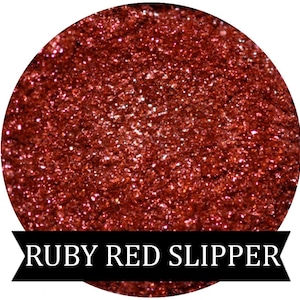May include: A close-up of a red glitter eyeshadow with the text "RUBY RED SLIPPER" below.