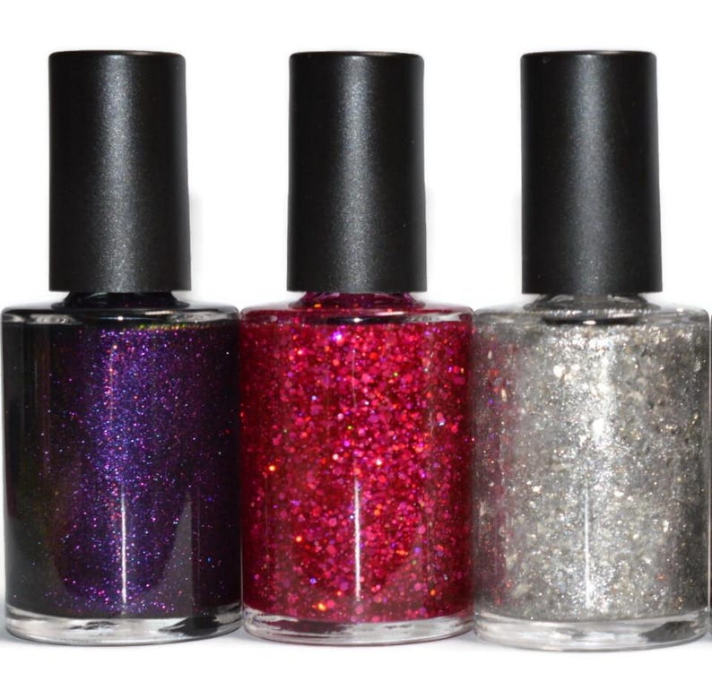 May include: Three nail polish bottles with black caps. The bottles contain purple, red, and silver glitter polish. The bottles are clear, allowing the color of the polish to be seen. The background is white.