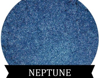 May include: A close-up of a blue iridescent glitter pigment. The pigment is in a round container and has a smooth, even texture. The text "NEPTUNE" is printed on a black ribbon below the container.