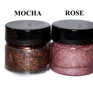 May include: Two small jars of glitter, one labeled "Mocha" and the other labeled "Rose". The glitter in the Mocha jar is a dark brown with iridescent shimmer. The glitter in the Rose jar is a light pink with iridescent shimmer.
