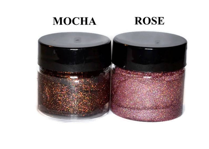 May include: Two small jars of glitter, one labeled "Mocha" and the other labeled "Rose". The glitter in the Mocha jar is a dark brown with iridescent shimmer. The glitter in the Rose jar is a light pink with iridescent shimmer.