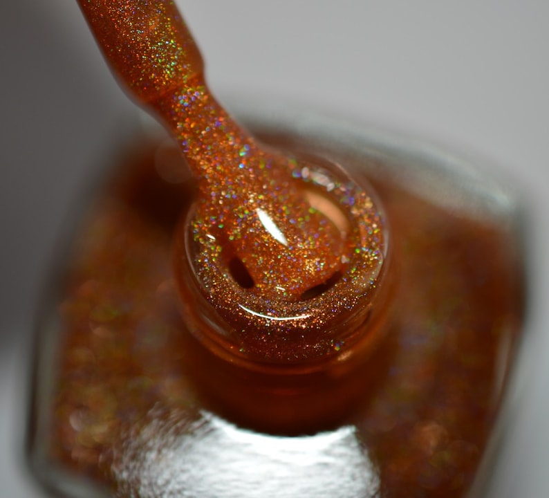May include: A close-up of a bottle of nail polish with a gold glitter finish. The bottle is open and the brush is dipped in the polish.