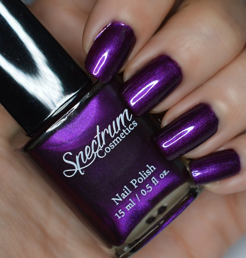 May include: A bottle of Spectrum Cosmetics nail polish in a deep purple color with a metallic finish. The bottle is labeled 'Spectrum Cosmetics' and 'Nail Polish' with the size '15 ml / 0.5 fl oz.'