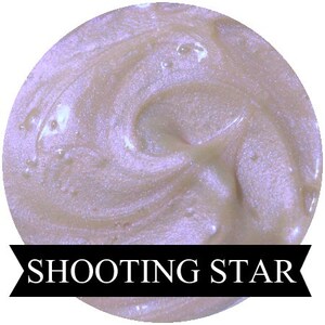 May include: A close-up of a shimmering, iridescent purple and white cosmetic product with a swirl pattern. The product is labeled "Shooting Star".