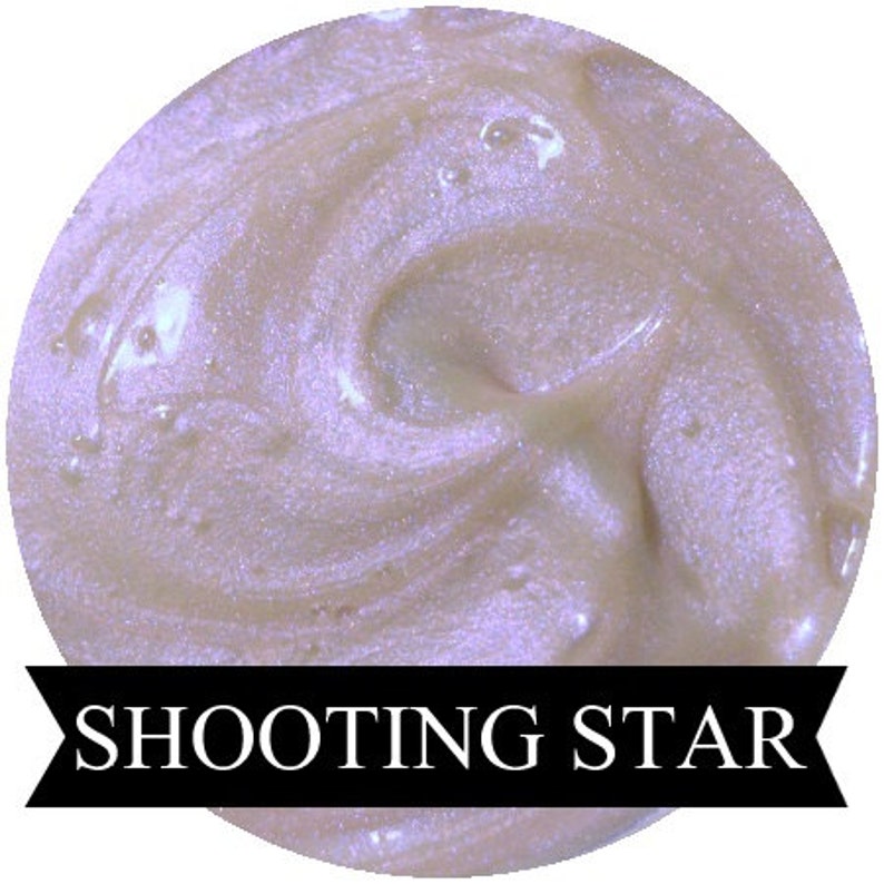 May include: A close-up of a shimmering, iridescent purple and white cosmetic product with a swirl pattern. The product is labeled "Shooting Star".