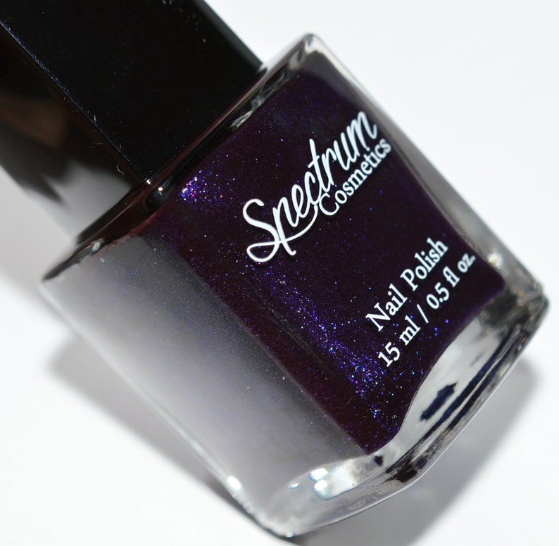May include: A bottle of Spectrum Cosmetics nail polish in a deep purple colour with a shimmer finish. The bottle is labelled "Nail Polish" and "15 ml / 0.5 fl oz".