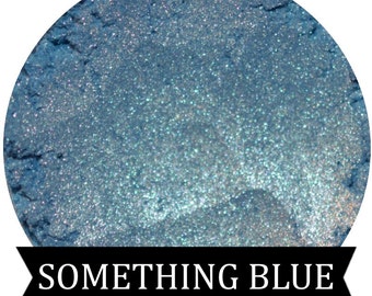 May include: A close-up of a blue iridescent mica powder. The powder is shimmery and has a fine texture. The text "SOMETHING BLUE" is printed below the powder.