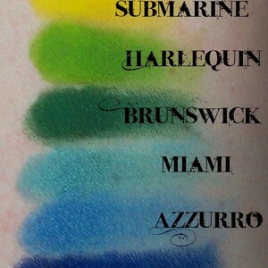 May include: A close-up of a makeup palette with 10 eyeshadows. The eyeshadows are arranged in a vertical row, with the names of each shade printed below them. The shades are: Fatality, Tangelo, Atomic, Submarine, Harlequin, Brunswick, Miami, Azzurro, Ferric, and Poe.