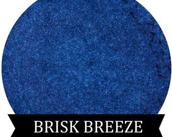 May include: A close-up of a deep blue mica powder with a shimmery finish. The powder is labeled "BRISK BREEZE".