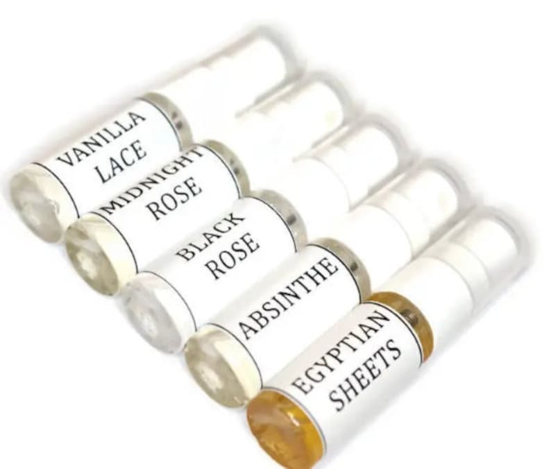 May include: Six small glass bottles with white labels and black text. The labels read "Vanilla Lace", "Midnight Rose", "Black Rose", "Absinthe", and "Egyptian Sheets".