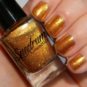 May include: A bottle of Spectrum Cosmetics nail polish in a gold glitter finish. The bottle is clear and shows the polish inside. The polish is a bright, metallic gold color with a fine glitter.
