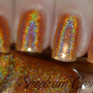 May include: Close-up of a bottle of gold glitter nail polish with a holographic finish. The bottle is labeled "Spectrum Cosmetics".