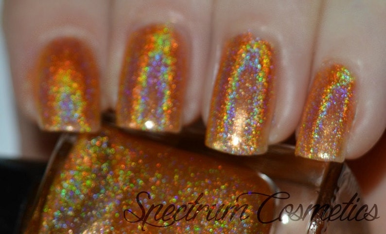 May include: Close-up of a bottle of gold glitter nail polish with a holographic finish. The bottle is labeled "Spectrum Cosmetics".