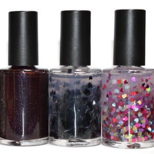 May include: Three nail polish bottles with black caps. The first bottle contains a dark, glittery polish. The second has black heart-shaped glitter. The third has colorful heart-shaped glitter.