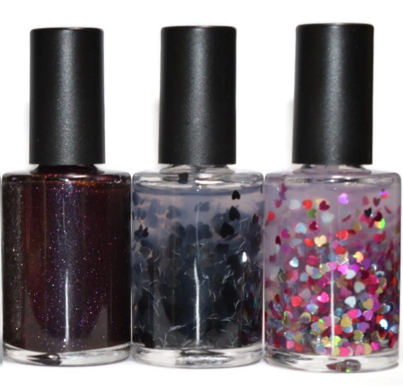 May include: Three nail polish bottles with black caps. The first bottle contains a dark, glittery polish. The second has black heart-shaped glitter. The third has colorful heart-shaped glitter.