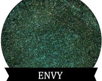 May include: A round, green eyeshadow with a shimmery finish. The eyeshadow is labeled "ENVY".